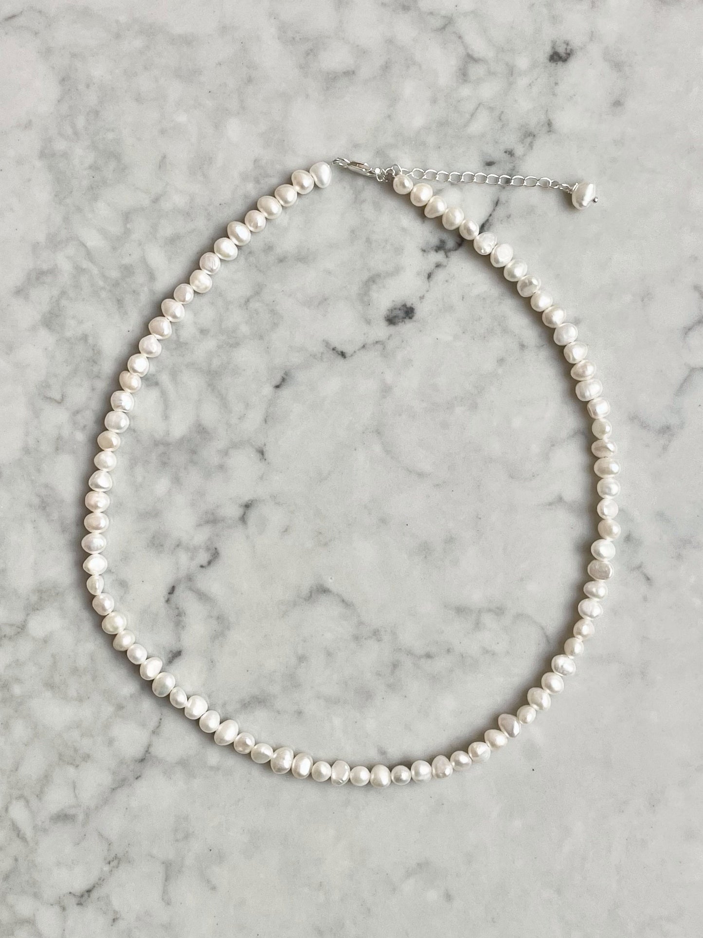 A freshwater pearl necklace with silver or gold-filled fittings, displayed on a marble surface.