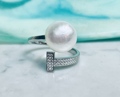 A white freshwater pearl ring with a sterling silver band and cubic zirconia accents, set against a backdrop of a turquoise fabric.
