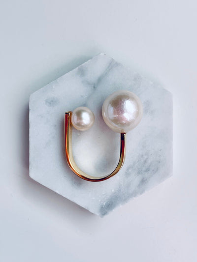 Pair of pearl earrings on a marble hexagonal stand against a light gray background