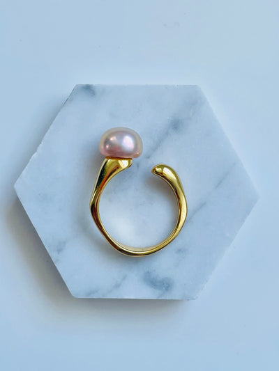 A ring with a pink freshwater pearl set on a gold vermeil band, displayed on a white marble surface.